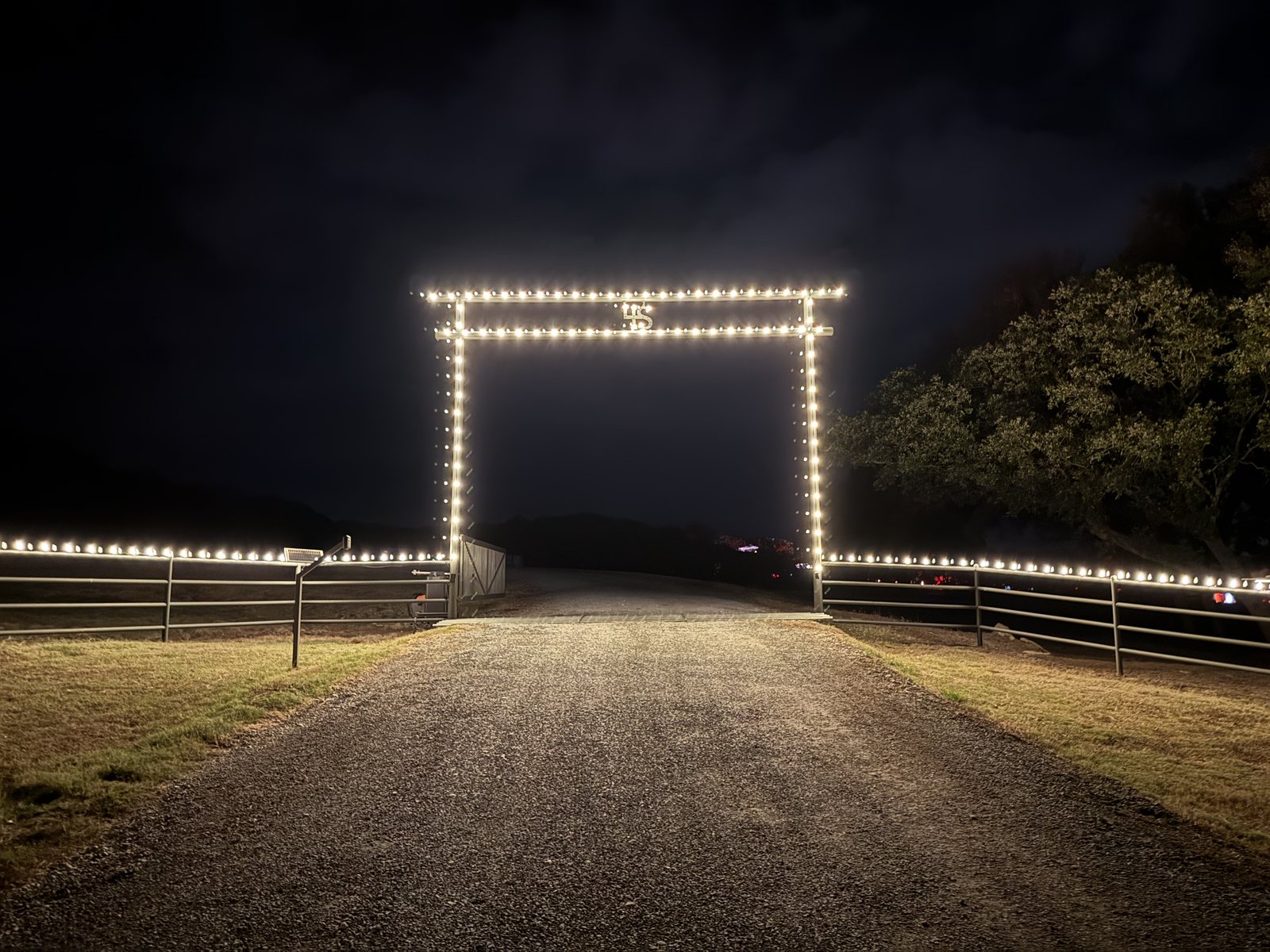 A ranch entrance gate and fence line outlined in warm white C9 lights at night
