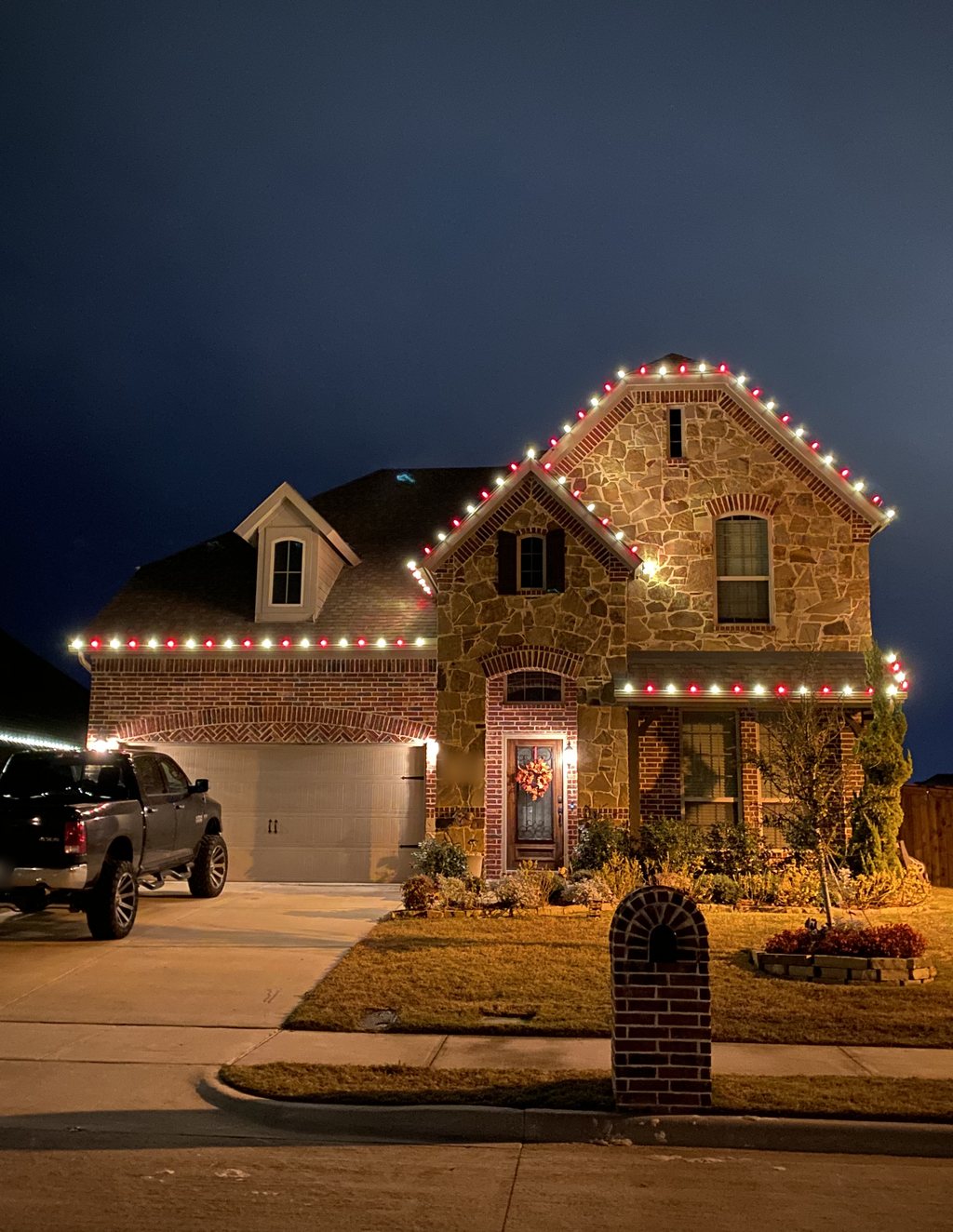 A two-story stone and brick home with alternating red and white C9 lights on every gable and eave